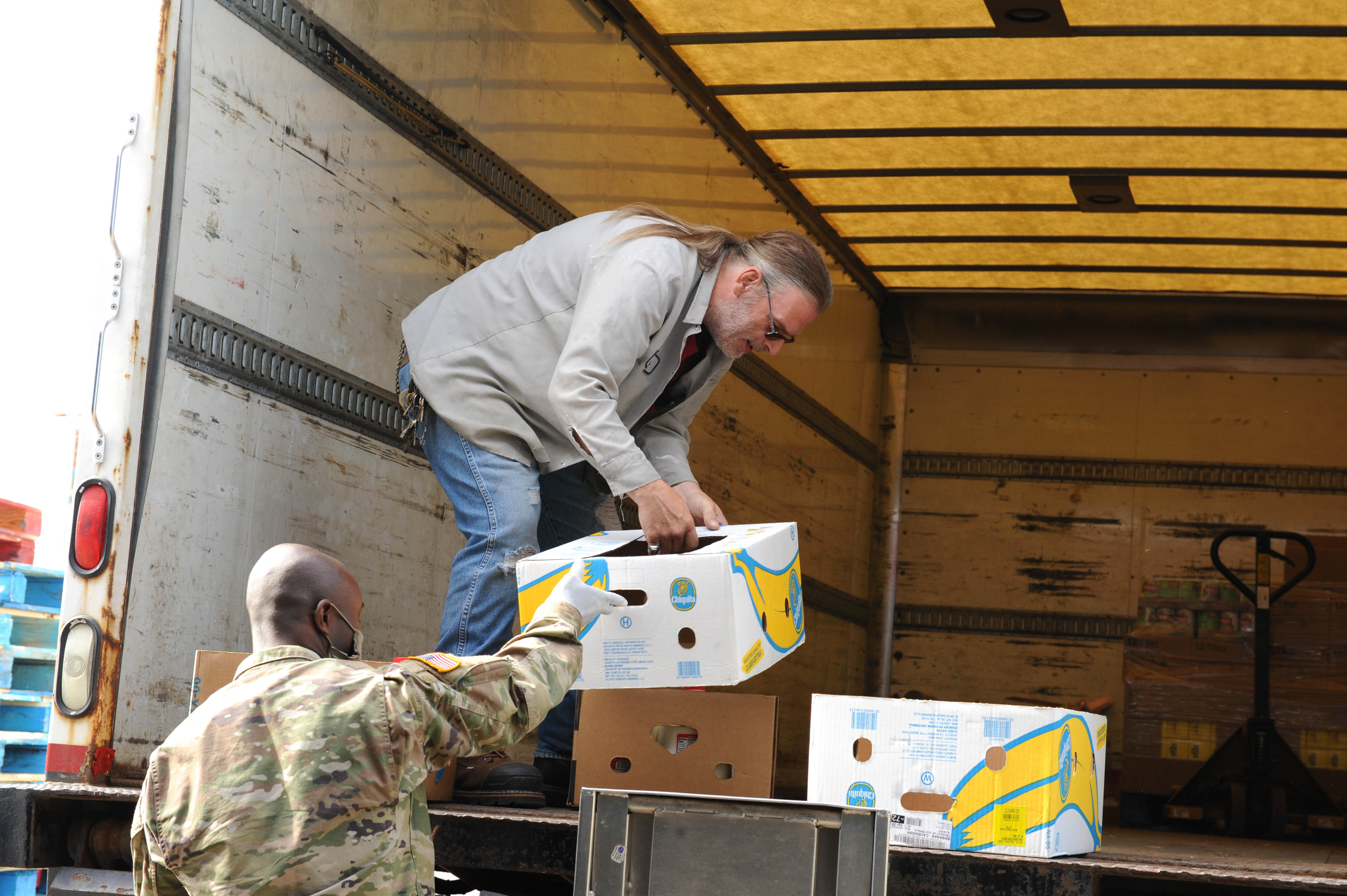 Soldier hands box of bananas to civilian helper in back of truck