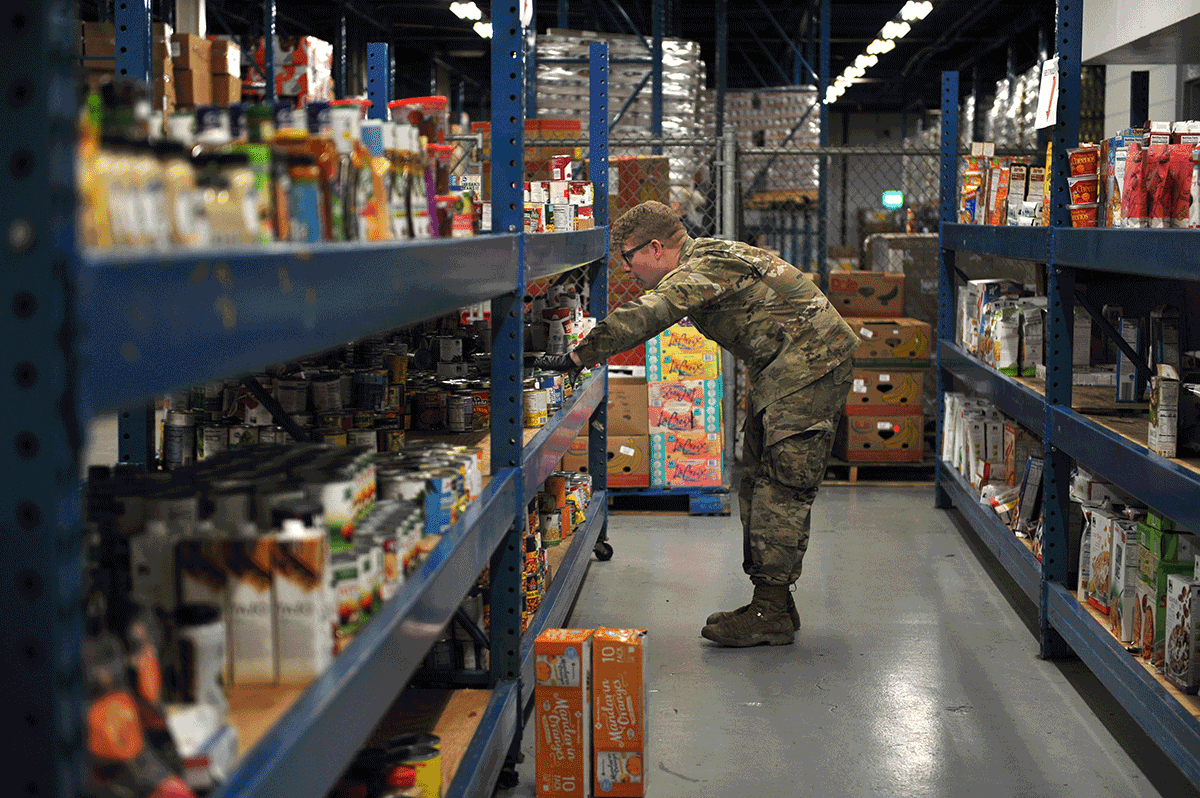 Soldier looking on shelf in isle in warehouse.