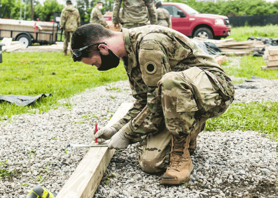 Soldier kneels to measure lumber.
