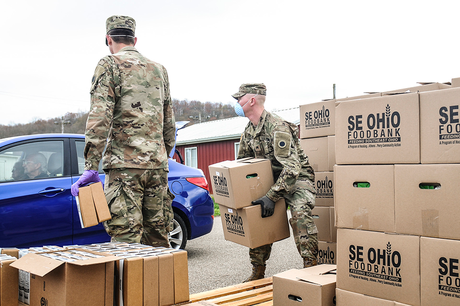 Soldiers pass out boxes of groceries at drive through.