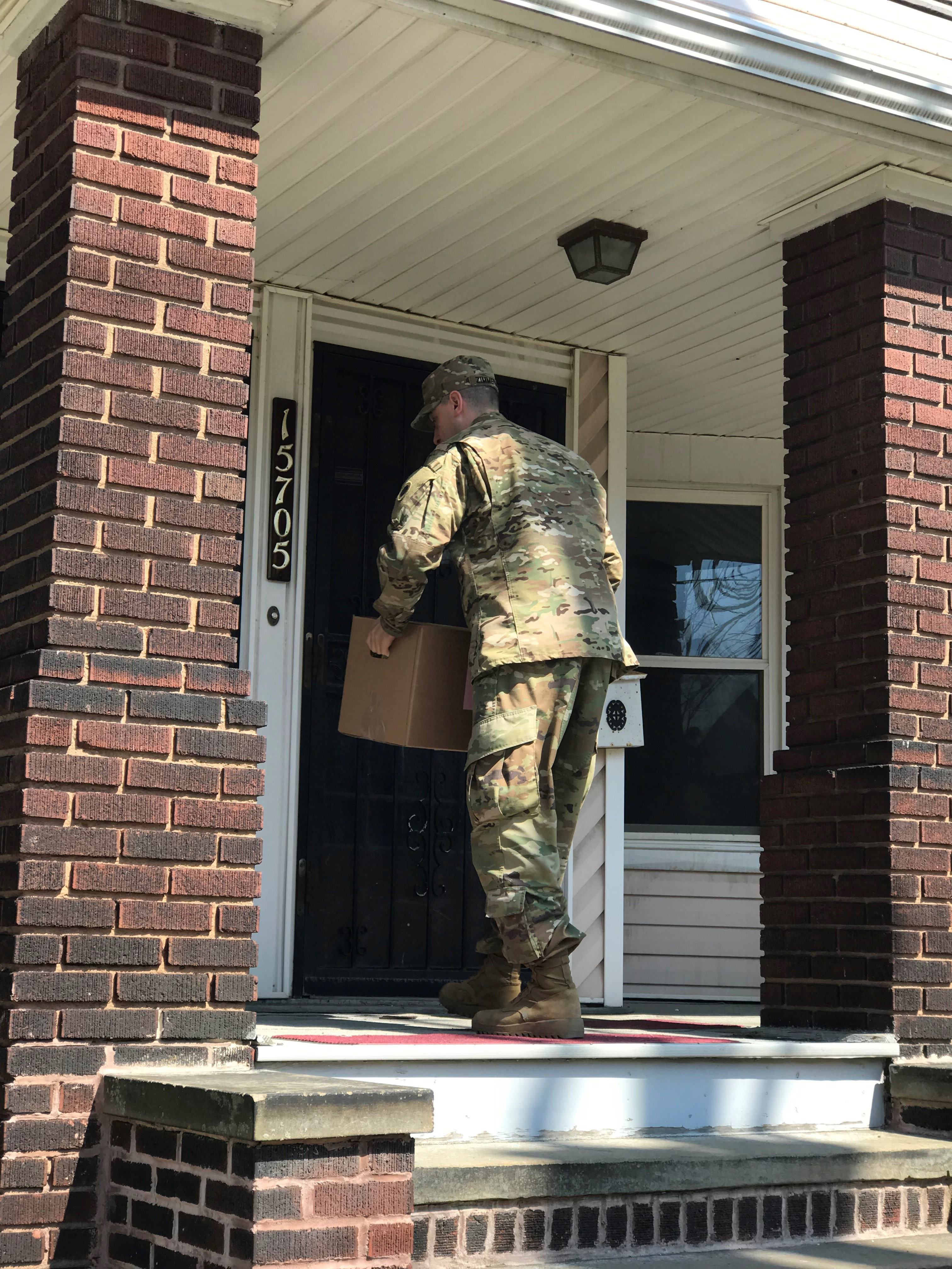 Soldier delivers groceries to porch.